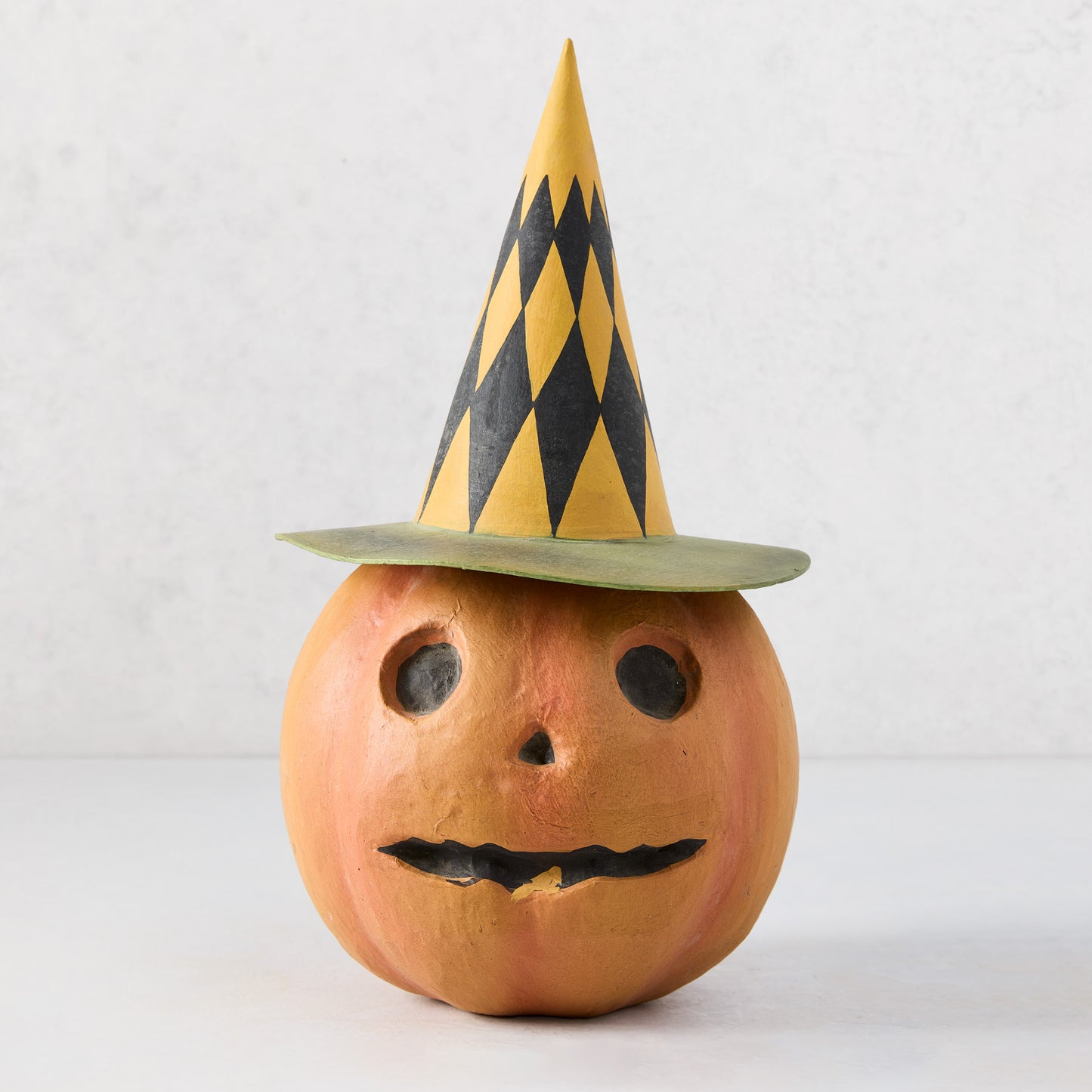 Vintage papier-mâché pumpkin candy bucket wearing a yellow and black diamond-patterned witch hat, 12 inches tall.