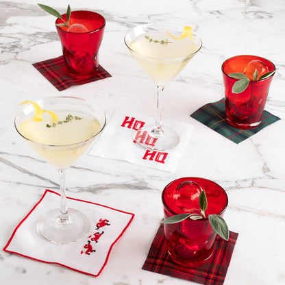Clear glass Midtown Martini glasses with cocktails, red tumblers, and holiday coasters on marble.