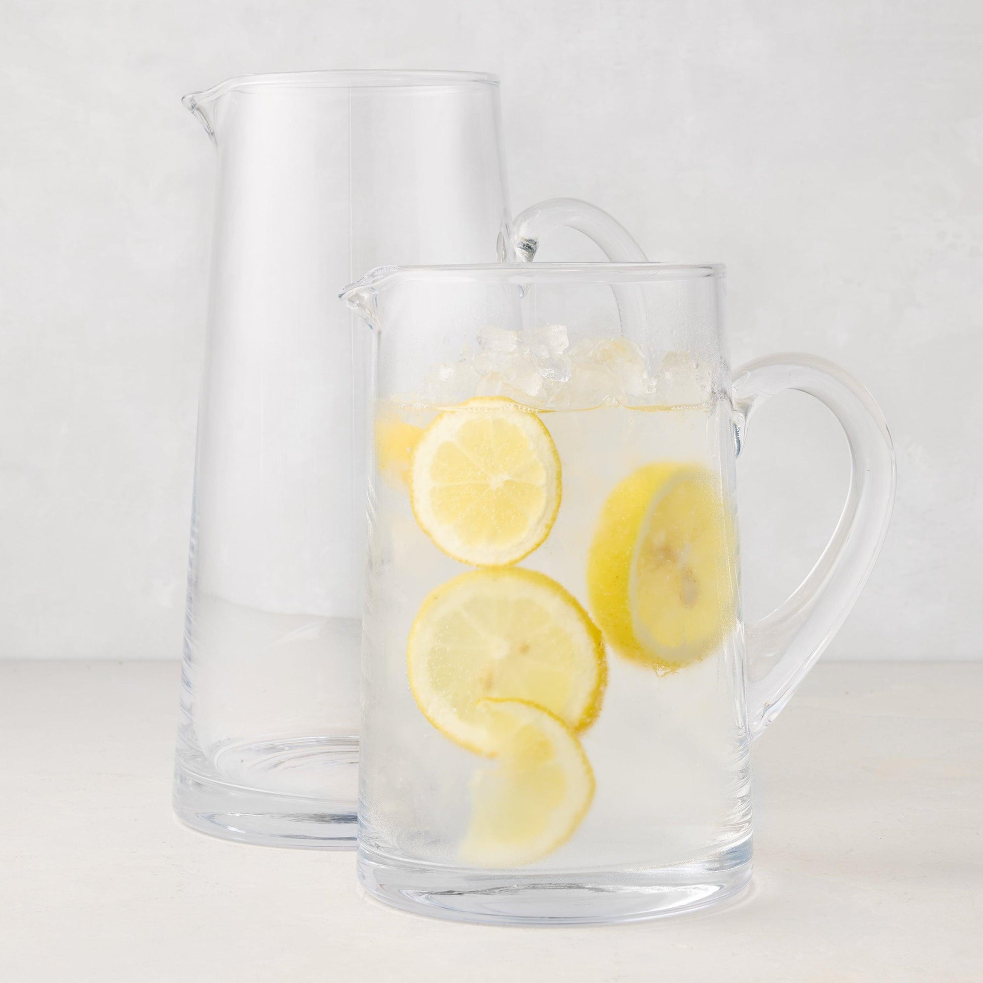 Two clear Midtown Tapered Glass Pitchers, one empty and one filled with lemonade and ice.