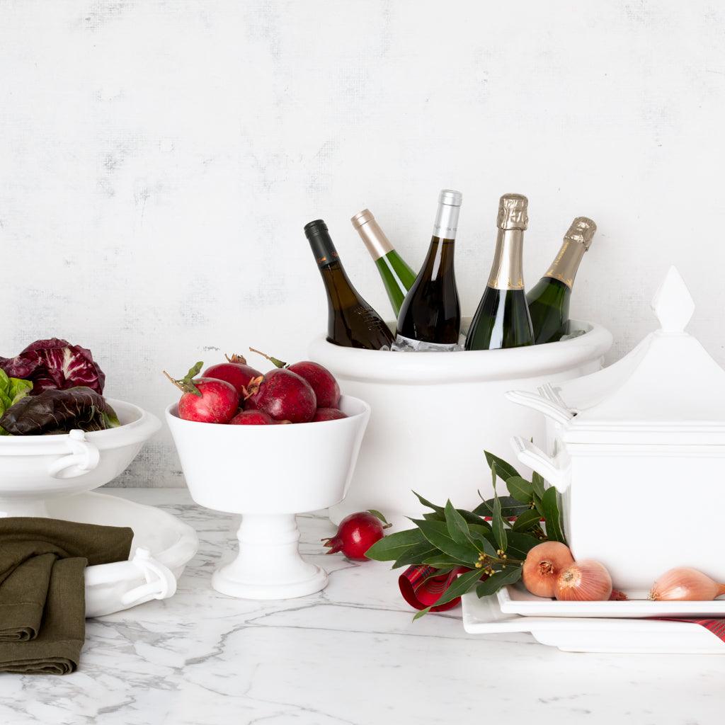 White ceramic Milano Tureen with lid, a bowl of pomegranates, and wine bottles in a large cooler.