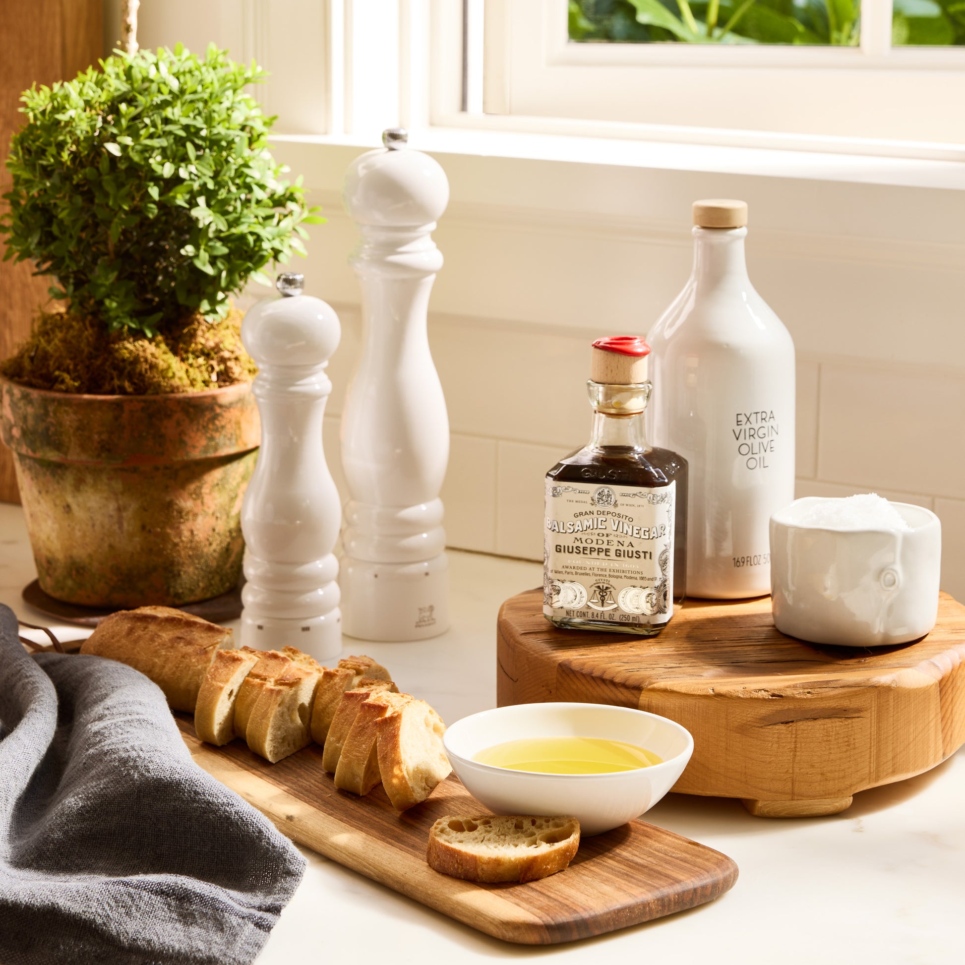 White ceramic dipping bowl with olive oil, baguette, and kitchen accessories.