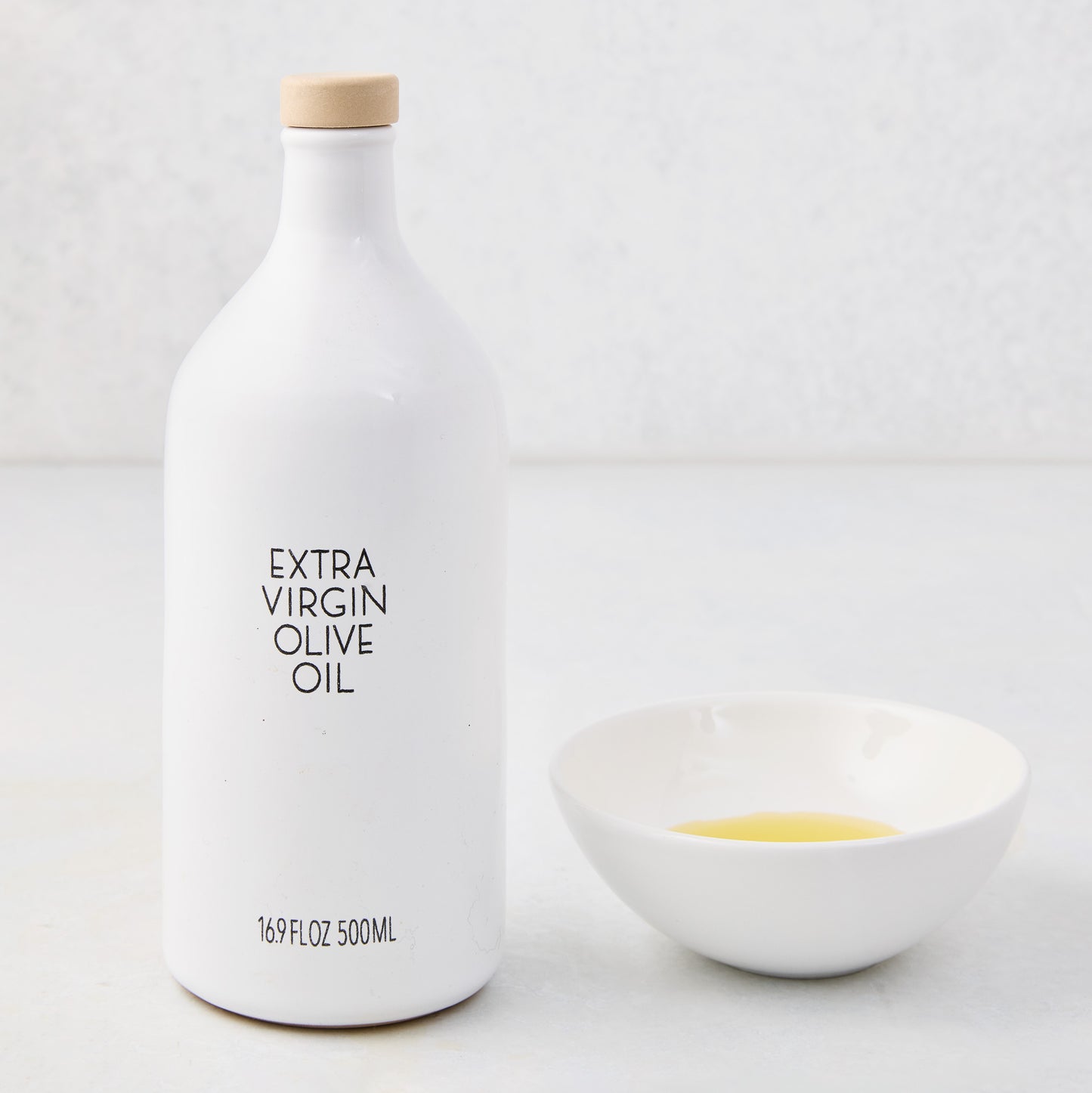 White ceramic dipping bowl with olive oil next to a white bottle of extra virgin olive oil.