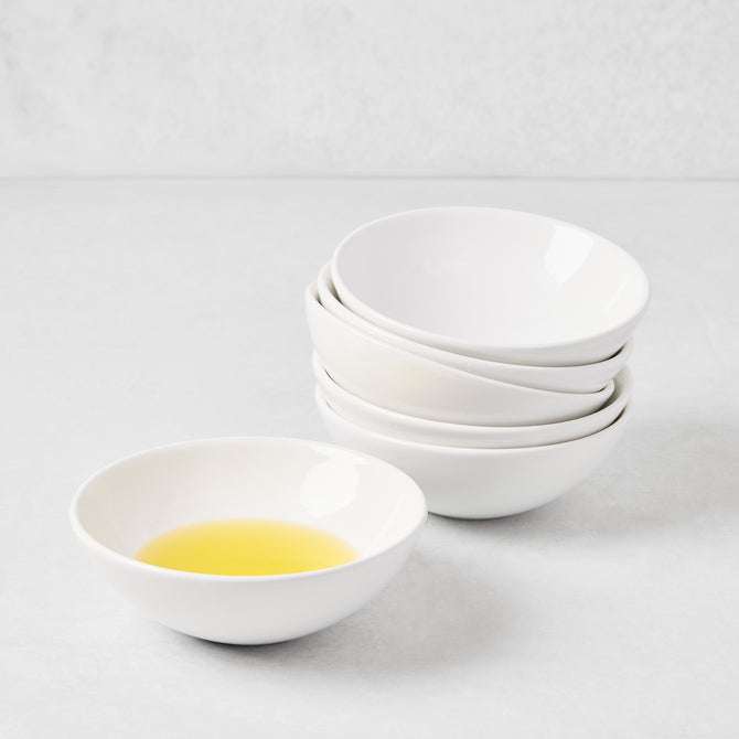 Creamy white ceramic dipping bowl with olive oil, stacked with four matching bowls.