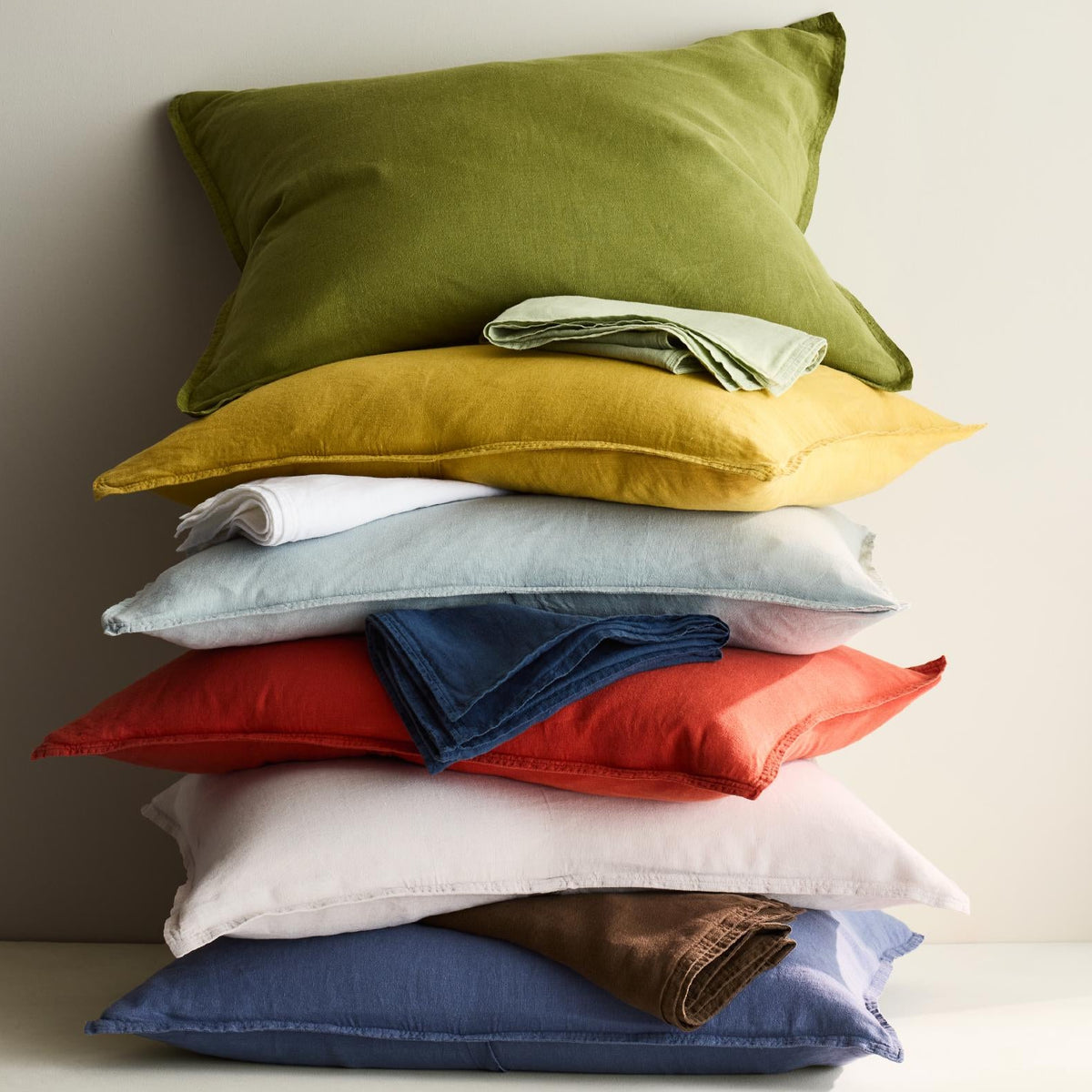 Stack of colorful European washed linen pillow shams in various shades including mint green, yellow, red, and blue.