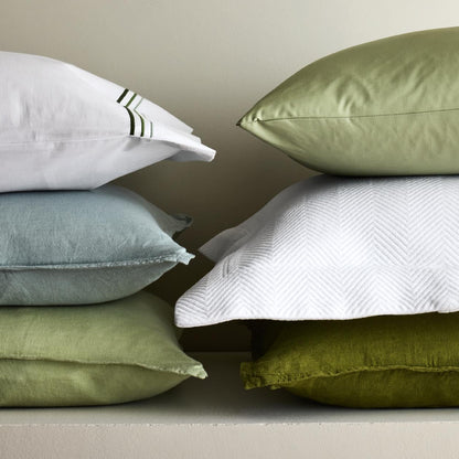 Stacked mint green, sage, and white linen and textured shams in various shades and weaves.