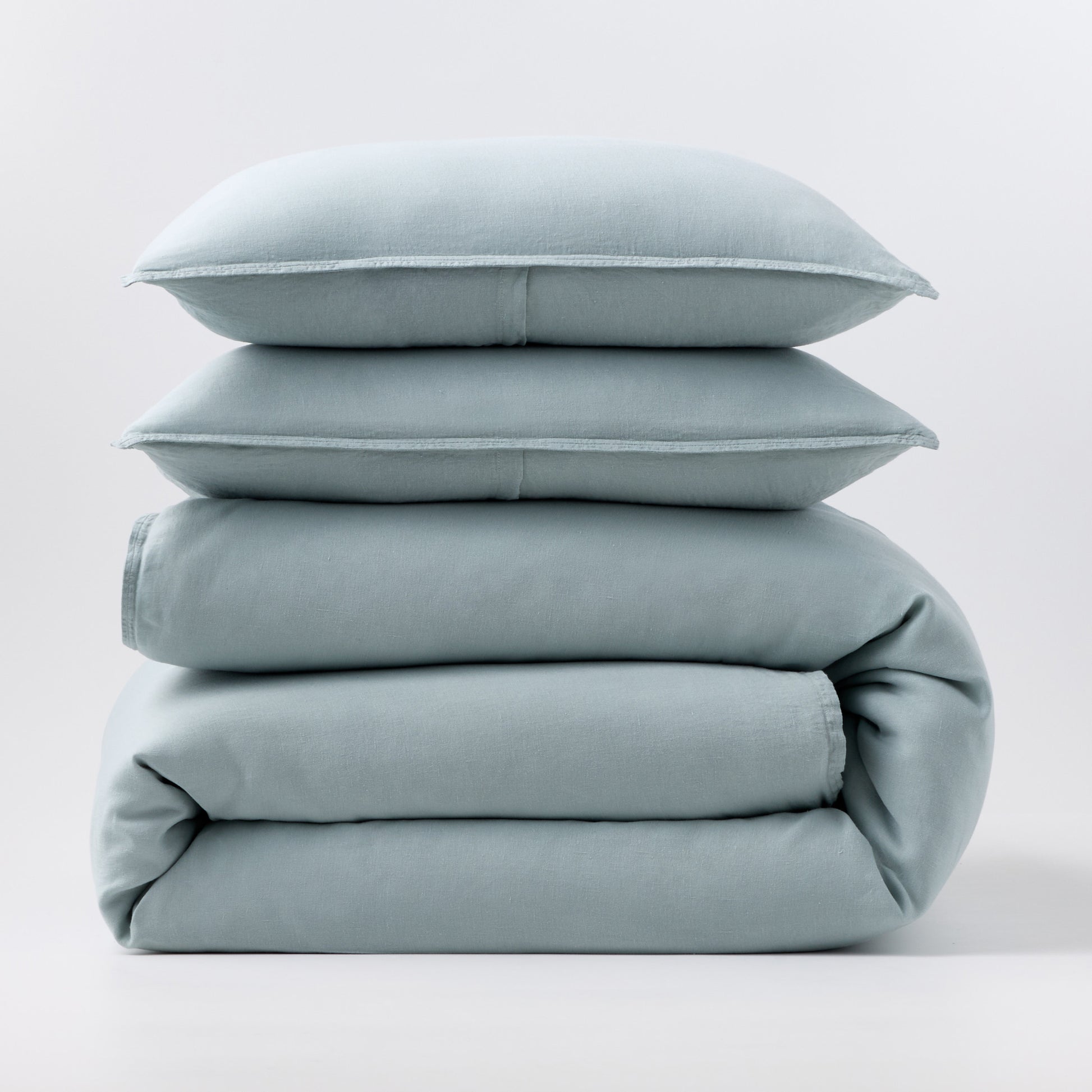 Stacked mist blue European washed linen duvet and two matching pillow shams on a white background.