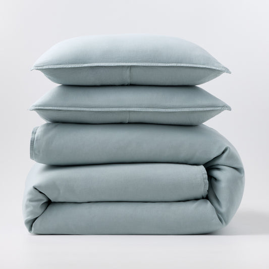 Stacked mist blue European washed linen duvet and two matching pillow shams on a white background.