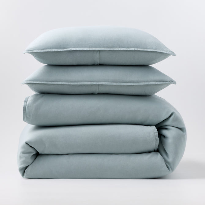 Stacked mist blue European washed linen duvet and two matching pillow shams on a white background.