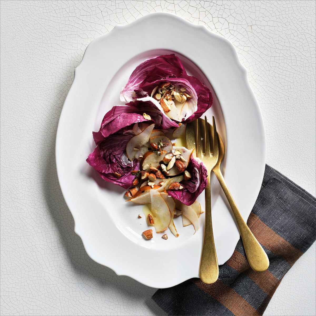 Large white ceramic Lungarno serving platter with softened edges, holding a radicchio and pear salad with gold utensils.