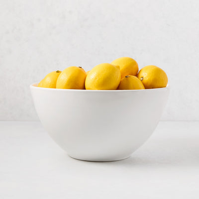 White ceramic serve bowl filled with bright yellow lemons.