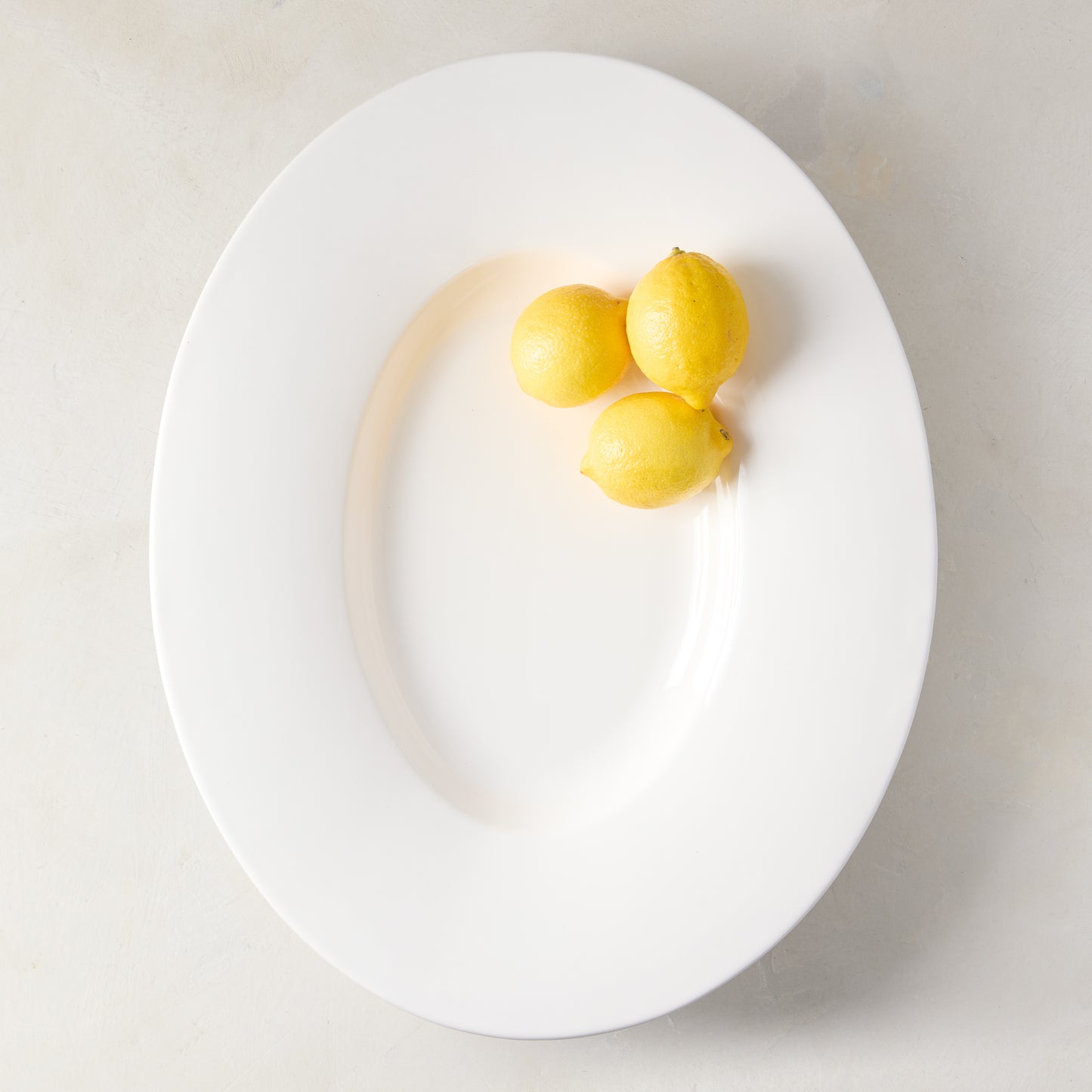 Modern oval wide-rim large ceramic platter with creamy glaze, featuring three lemons.