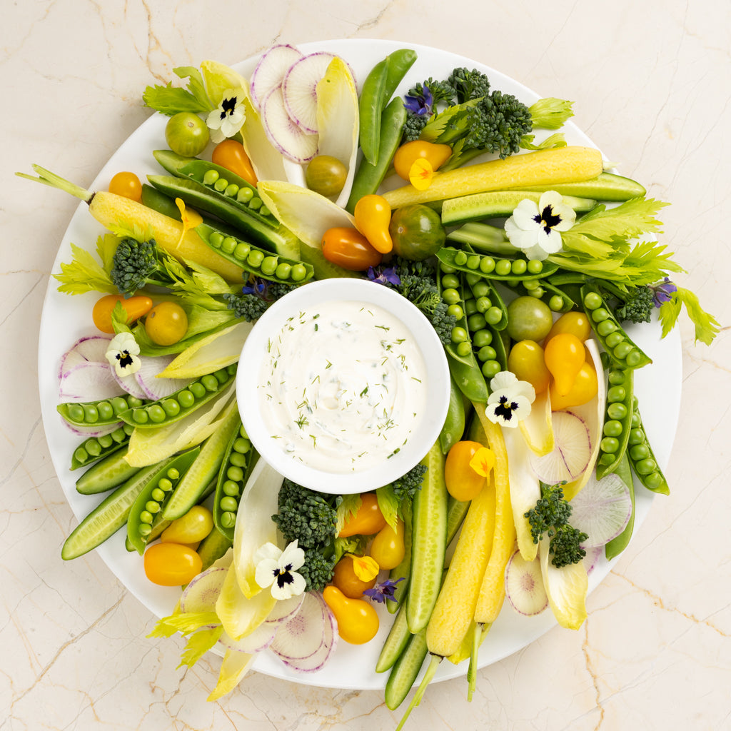White ceramic round serving platter with fresh vegetables and dip.