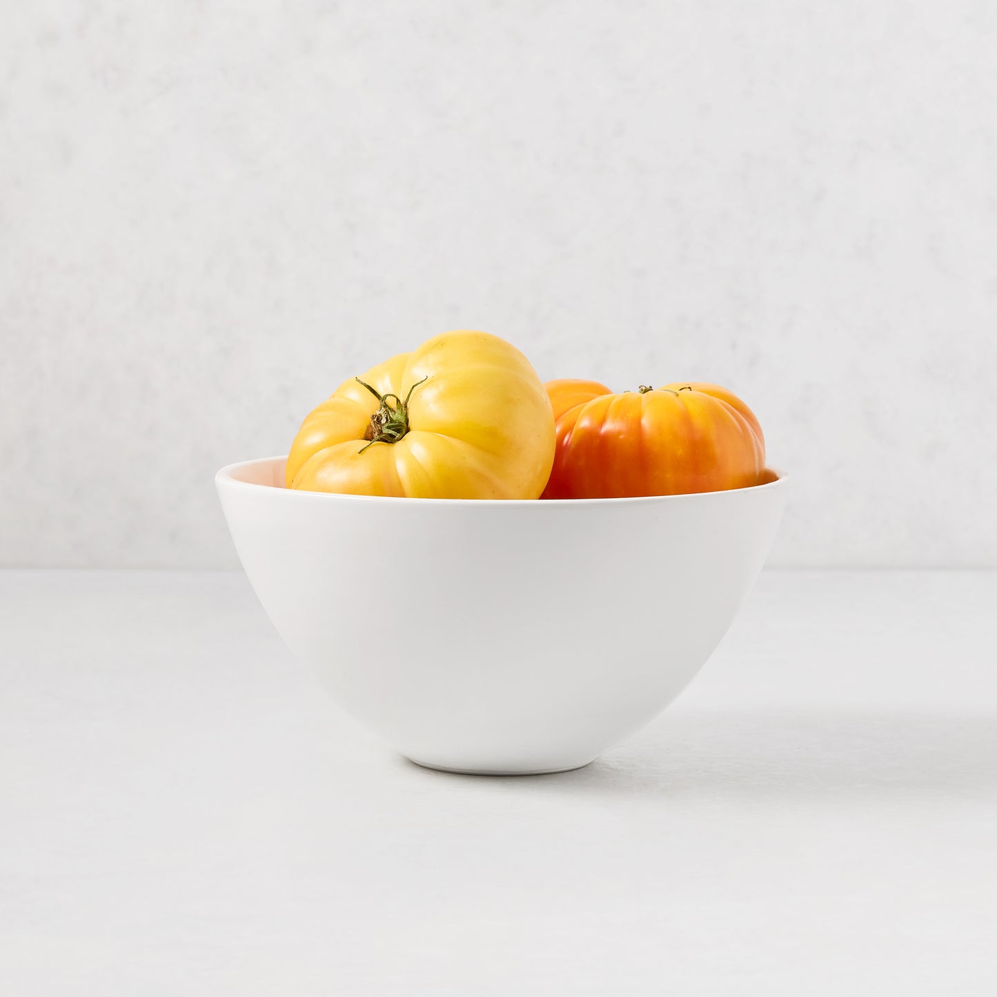 White ceramic HG Modern Small Serve Bowl with yellow and orange heirloom tomatoes.