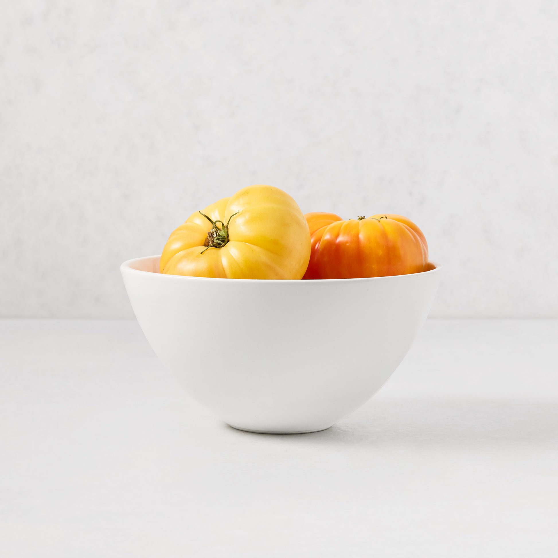White ceramic HG Modern Small Serve Bowl with yellow and orange heirloom tomatoes.