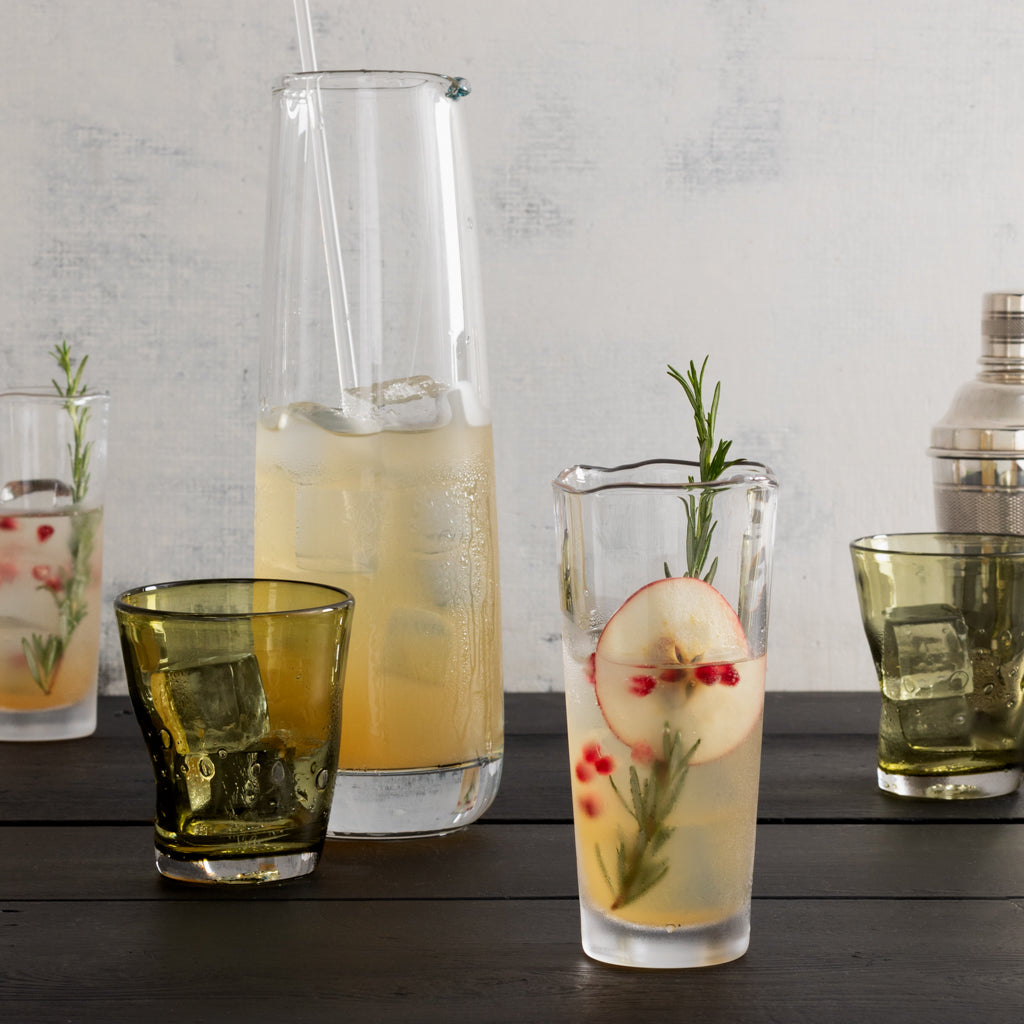 Clear Mozes scissor-cut water glass with a rippled rim, filled with a drink, apple slice, and rosemary.