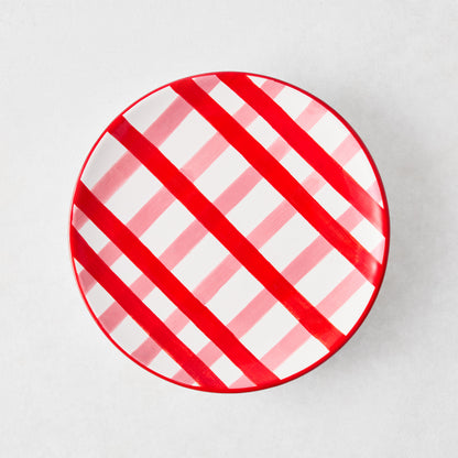 Round ceramic appetizer plate featuring a diagonal pink and red plaid pattern on a white background.