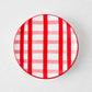 Round ceramic appetizer plate with a hand-painted red and pink plaid pattern on a white background.