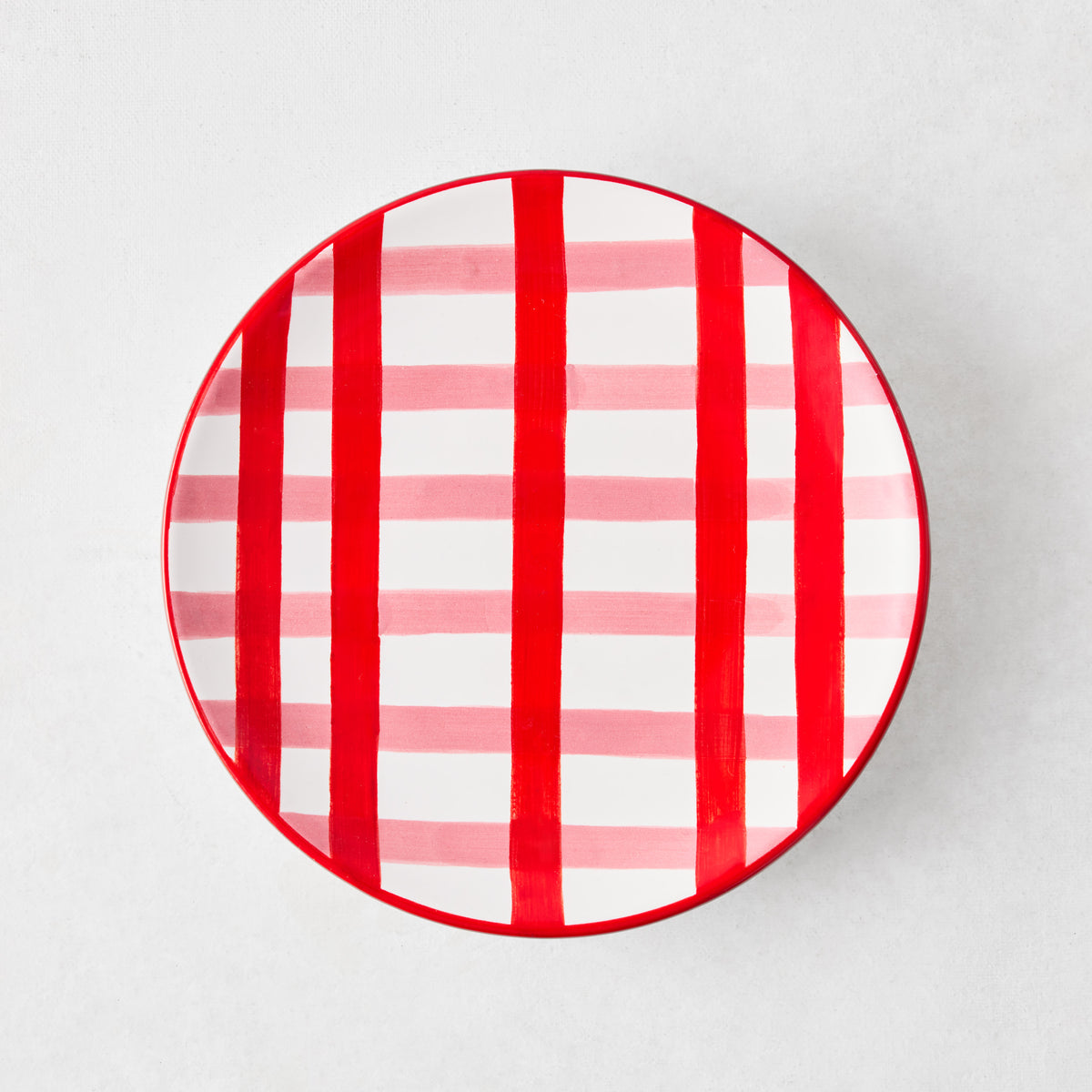 Round ceramic appetizer plate with a hand-painted red and pink plaid pattern on a white background.