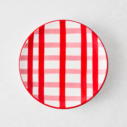 Round ceramic appetizer plate with a hand-painted red and pink plaid pattern on a white background.
