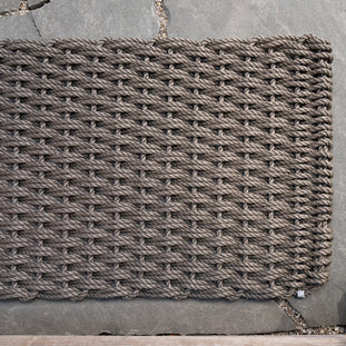 Mushroom Braided Rope Doormat, handwoven from thick, durable gray rope, on a stone patio.