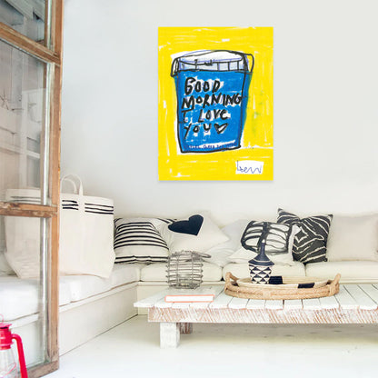 Kerri Rosenthal's "My First Love" art print, a vibrant blue cup on a yellow background, framed and hung above a white sofa.