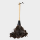 Natural feather duster with dark brown feathers, blond wood handle, black leather ferrule and hanging strap.