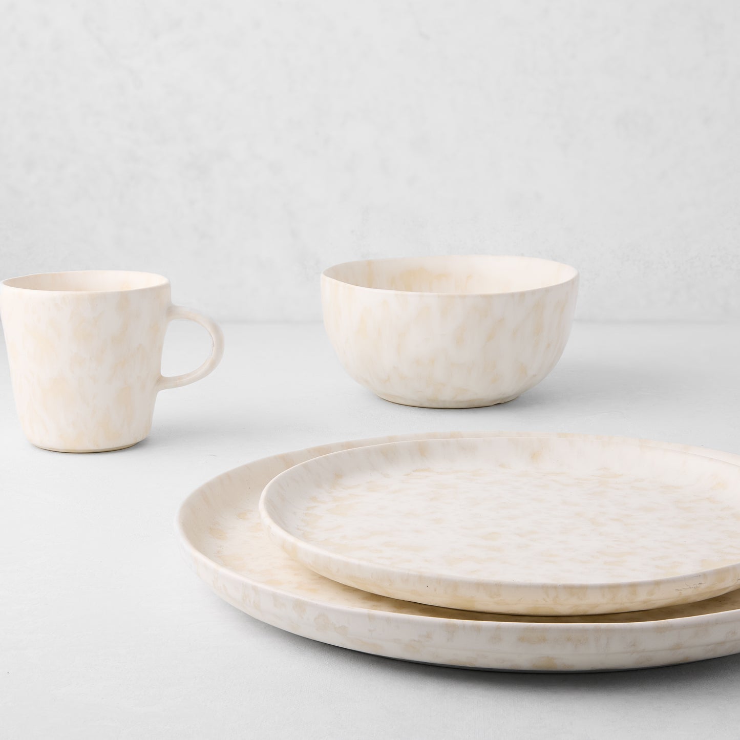 Natural Nuno Splatter stoneware dinner plate, salad plate, bowl, and mug with beige spots on a cream base.