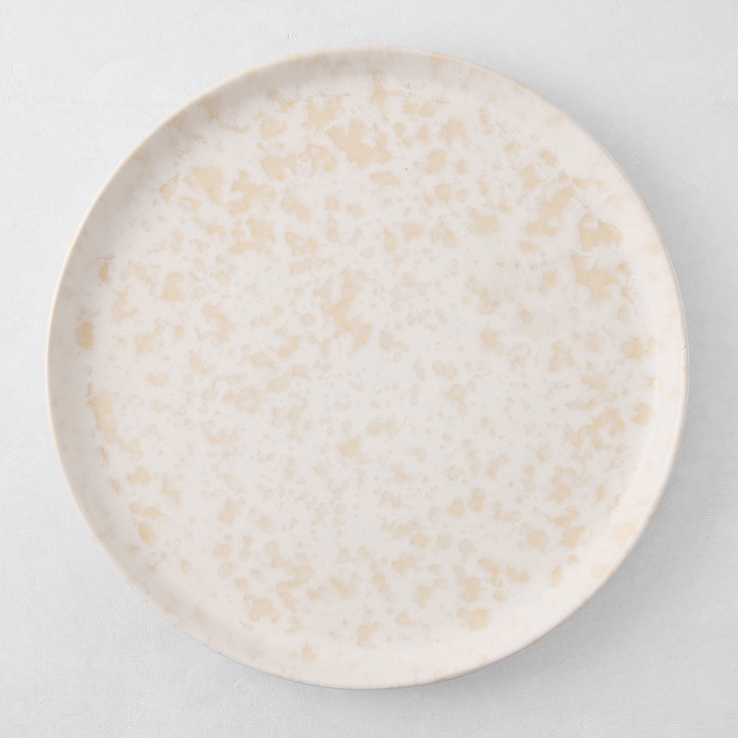 Natural Nuno Splatter 11" stoneware dinner plate with beige spots on a pale cream base.