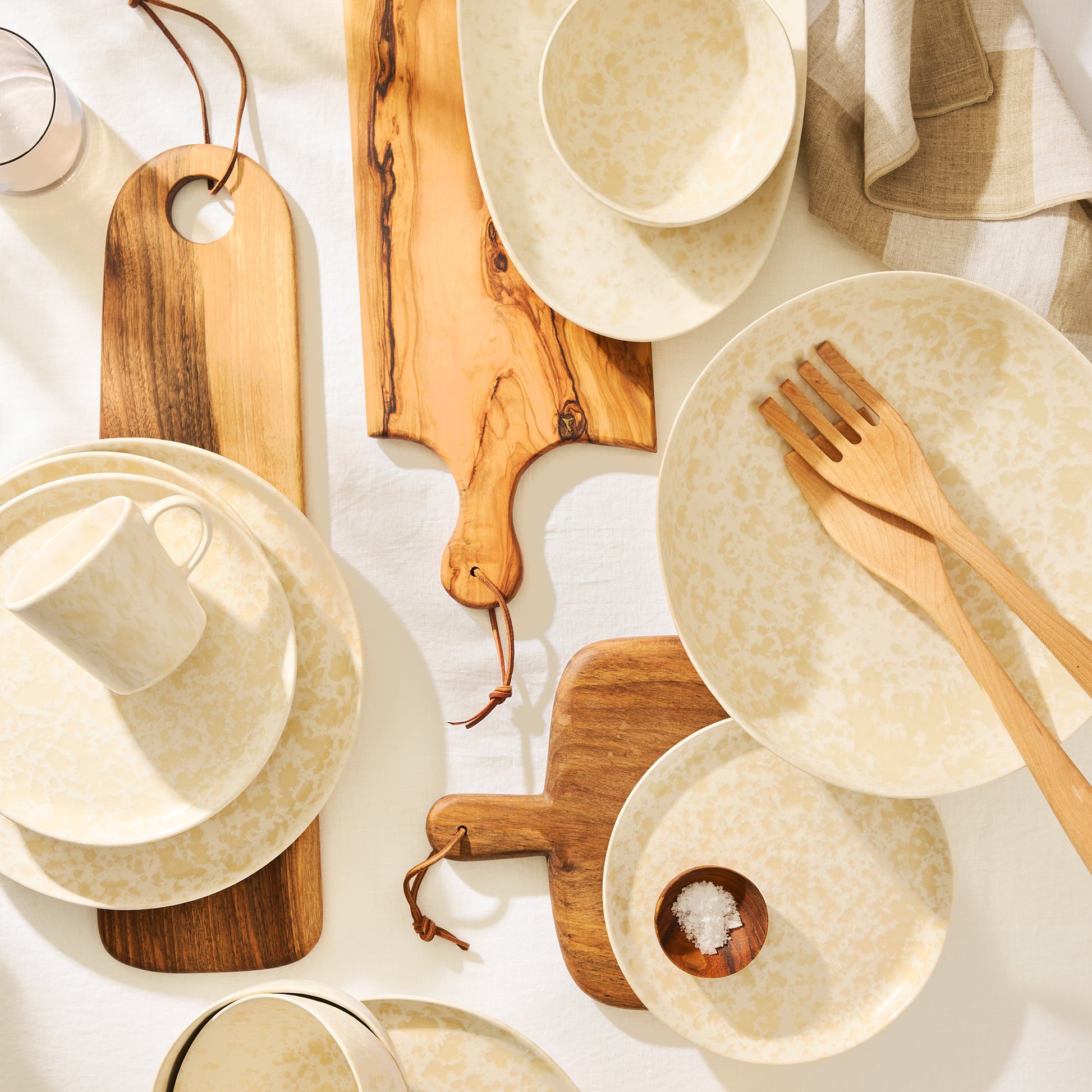 Natural Nuno Splatter stoneware serveware set with beige splatter on cream, wooden boards, and utensils.