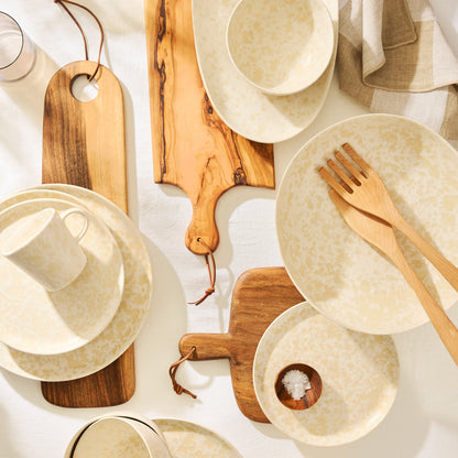 Natural Nuno Splatter stoneware serveware set with beige splatter on cream, wooden boards, and utensils.
