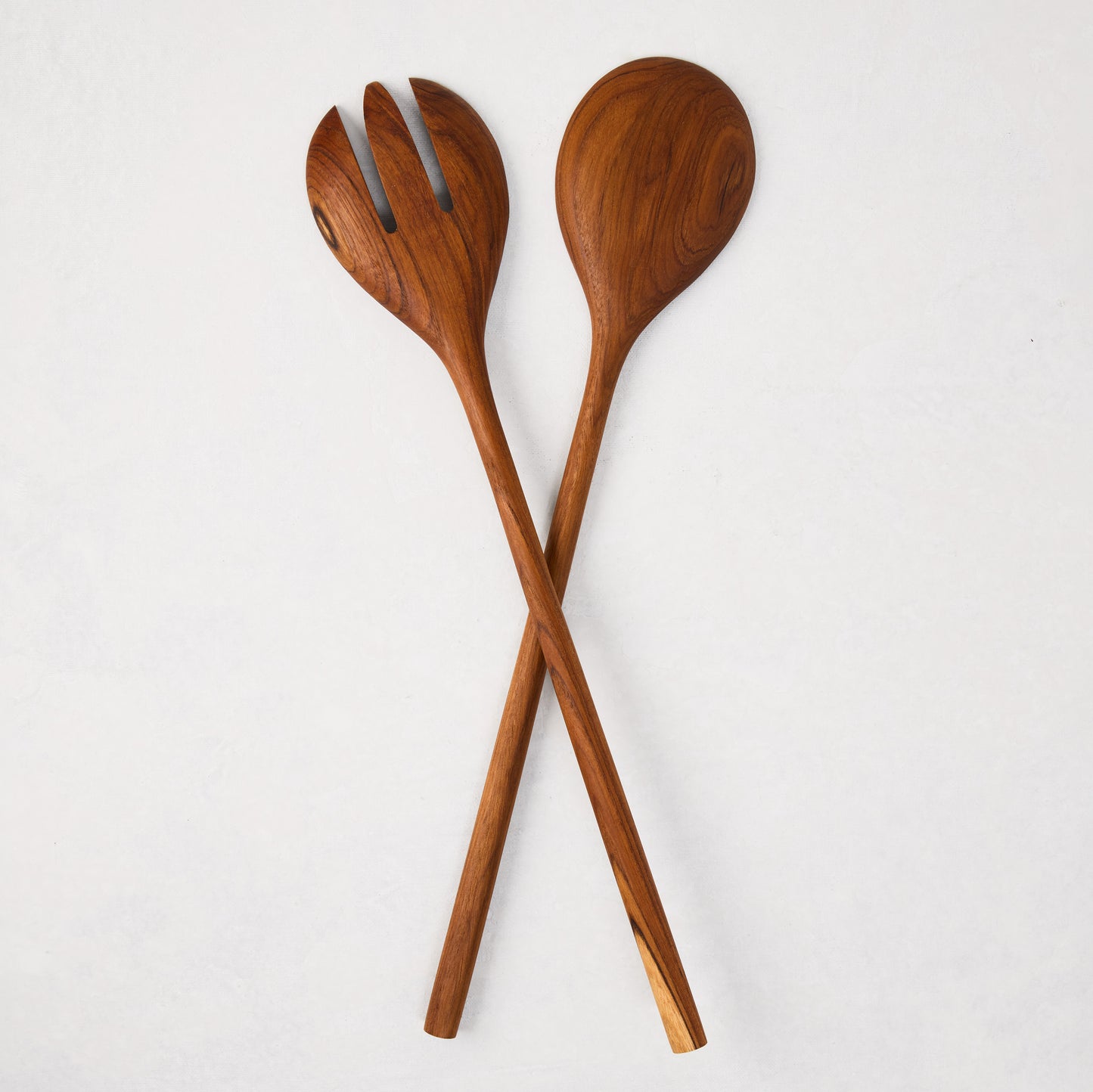 Natural teak wood long-handled 2-piece serving set, spoon and fork, crossed on white.