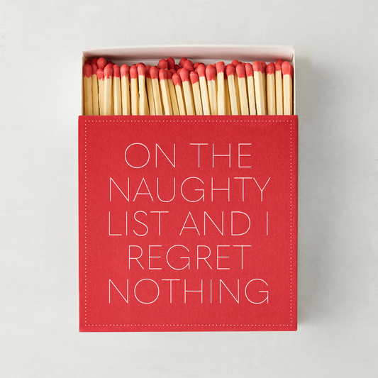 Red matchbox with white text reading On The Naughty List And I Regret Nothing, filled with oversized red-tipped matches.