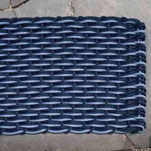 Navy and Glacier Bay braided rope doormat with a tight, woven pattern on a stone surface.