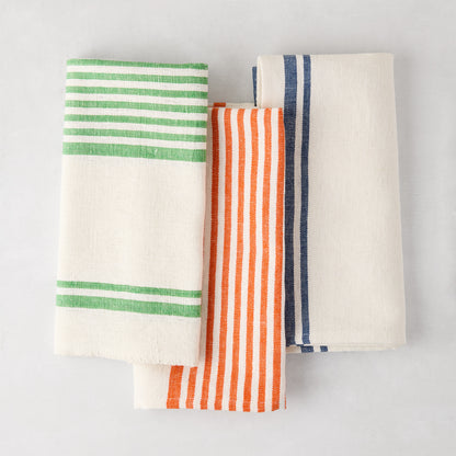 Three folded cotton-linen napkins: green, orange, and navy boat stripes on natural fabric.