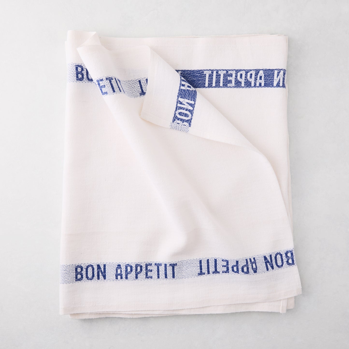 Folded white linen runner with "BON APPETIT" in navy blue text.