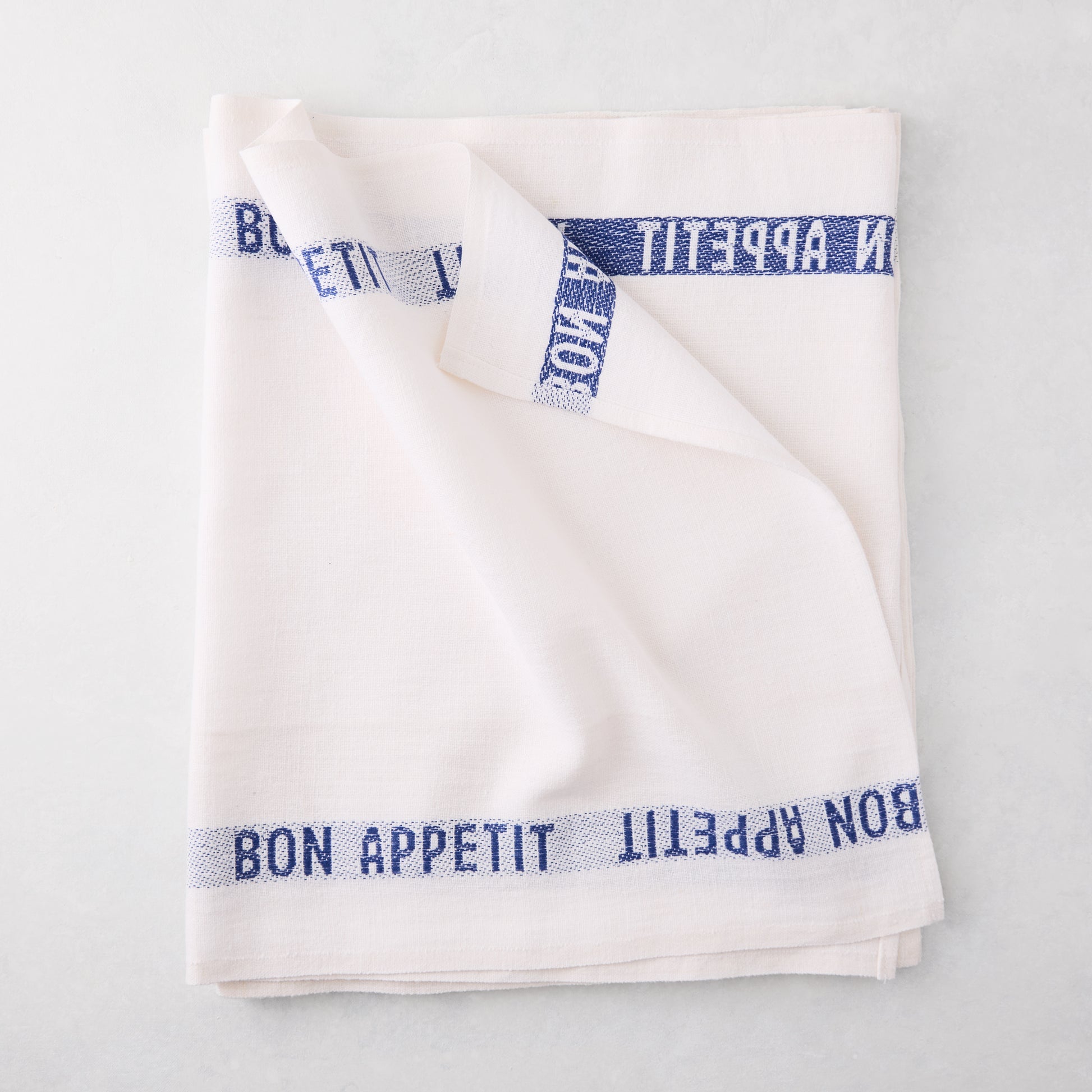 Folded white linen runner with "BON APPETIT" in navy blue text.