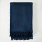 Folded navy blue cashmere throw blanket with classic fringe.