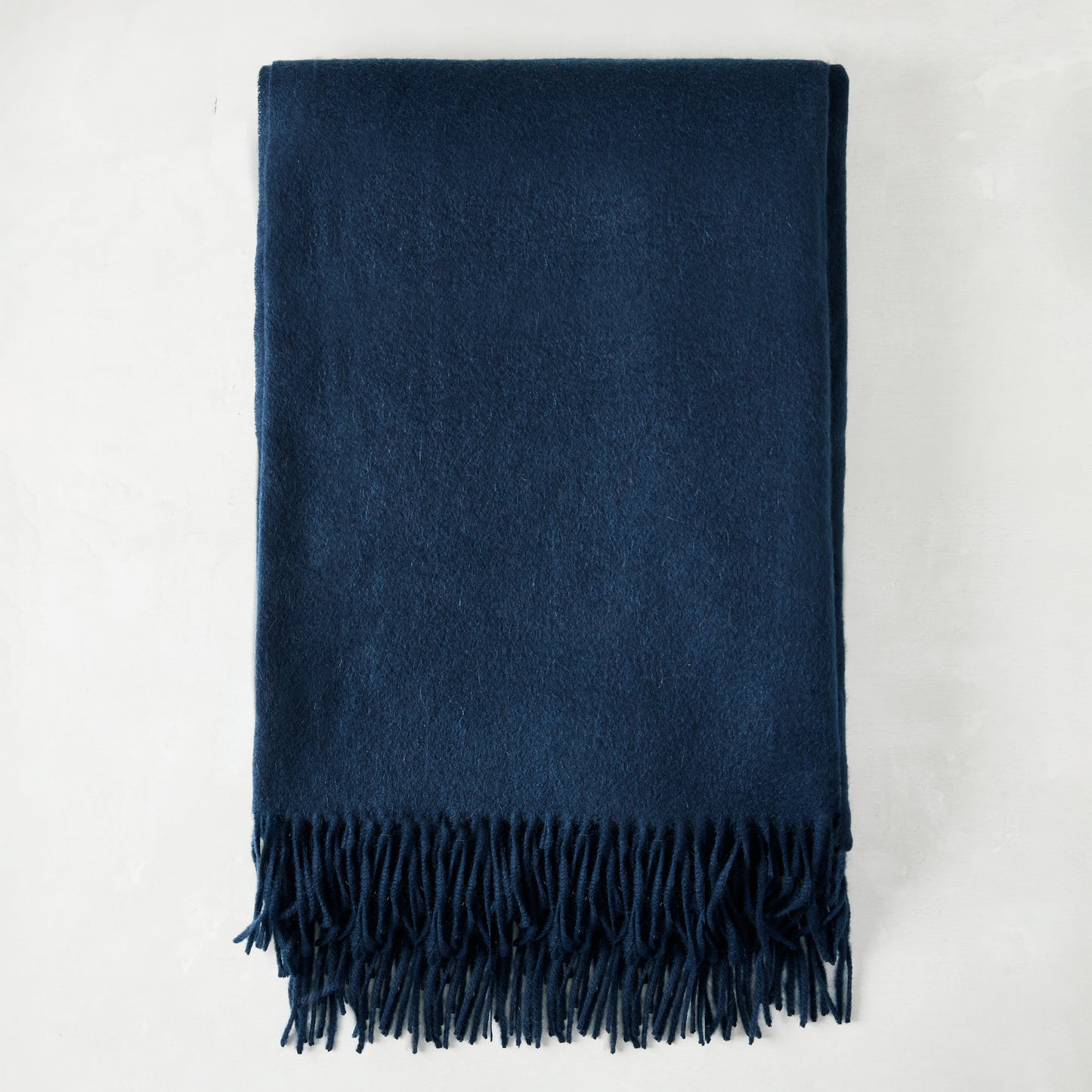 Folded navy blue cashmere throw blanket with classic fringe.