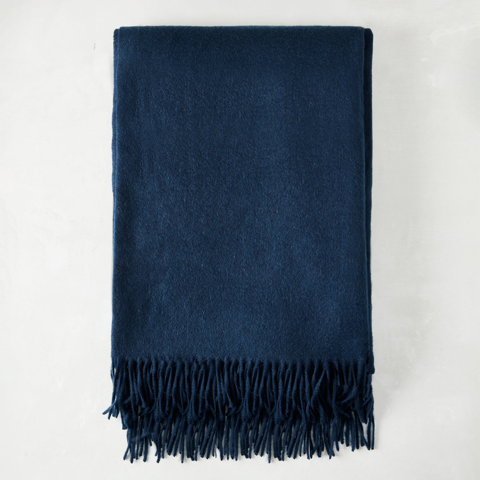 Folded navy blue cashmere throw blanket with classic fringe.