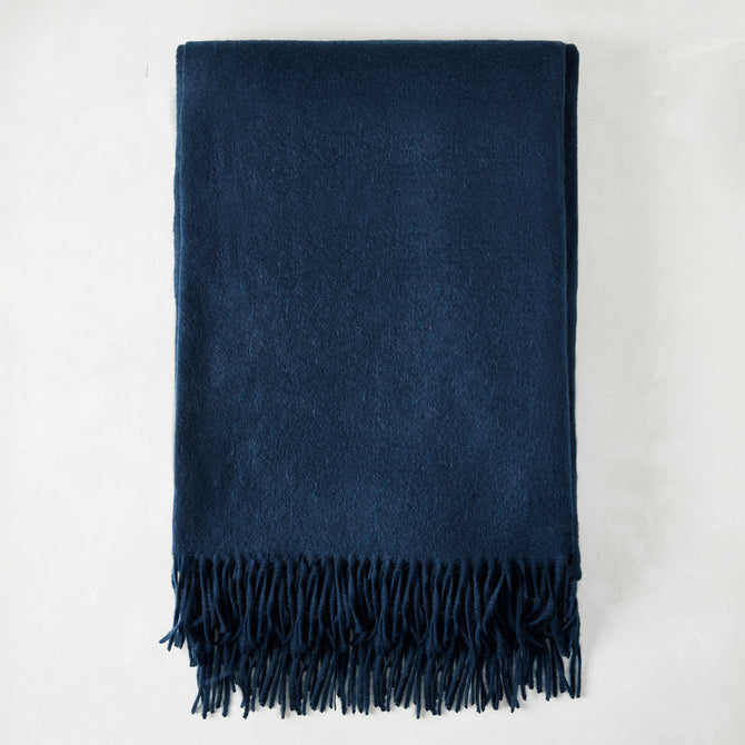 Folded navy blue cashmere throw blanket with classic fringe.