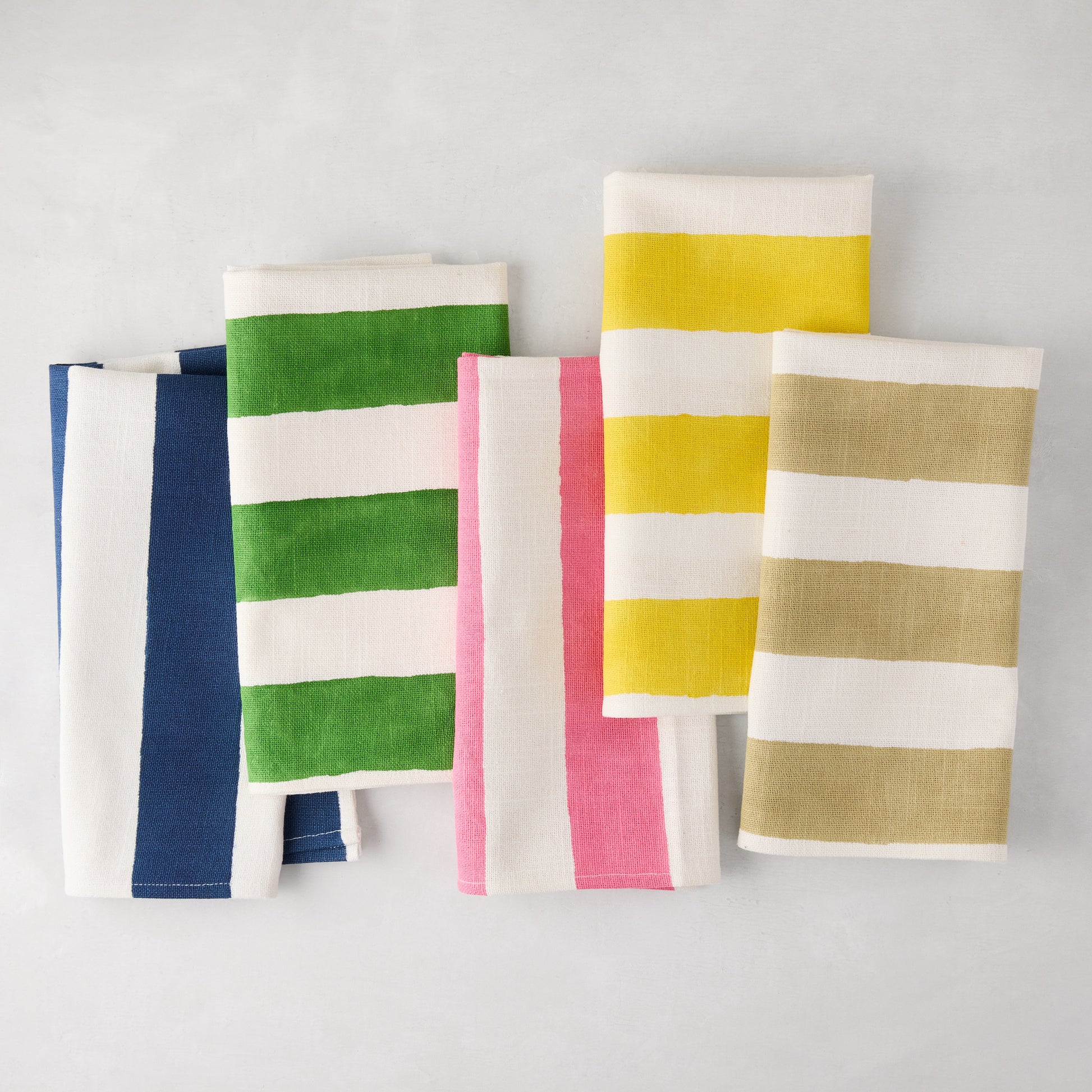 Five folded cotton napkins with thick white and colored stripes: navy, green, pink, yellow, and olive.