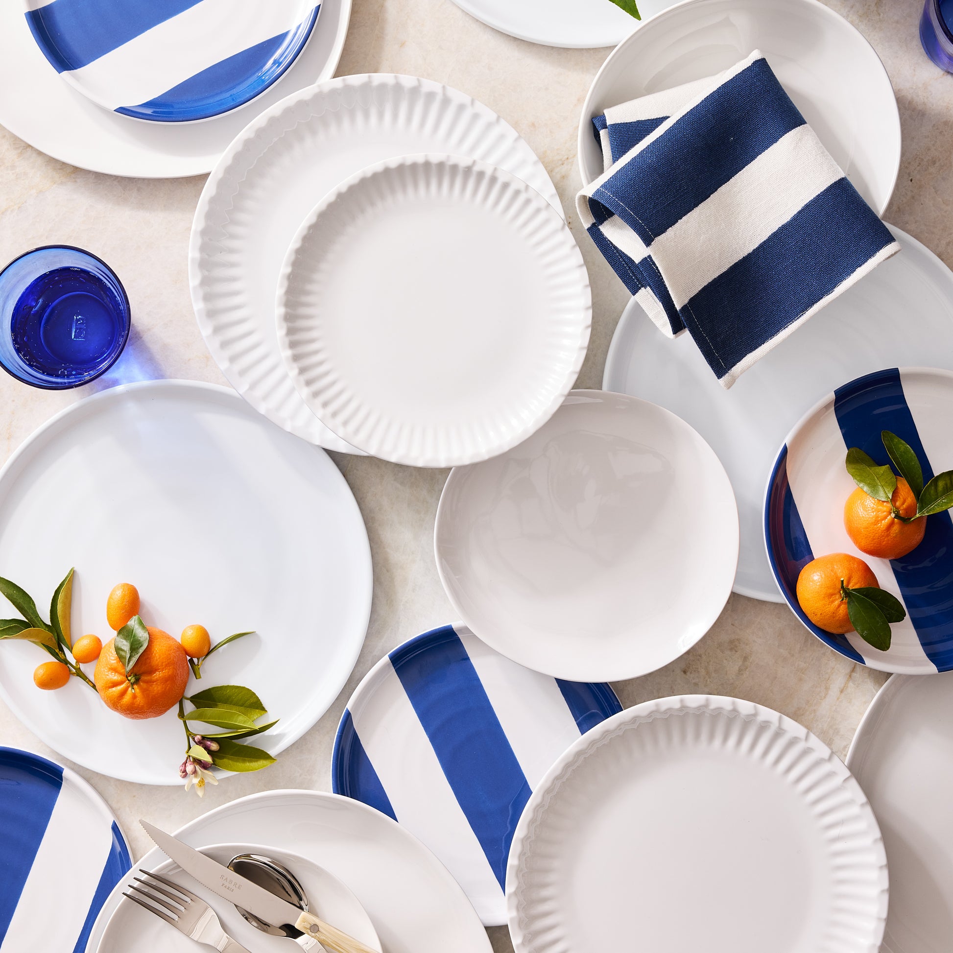 Navy Hampton Stripe Cotton Napkin folded on white plates with blue striped plates and tangerines.