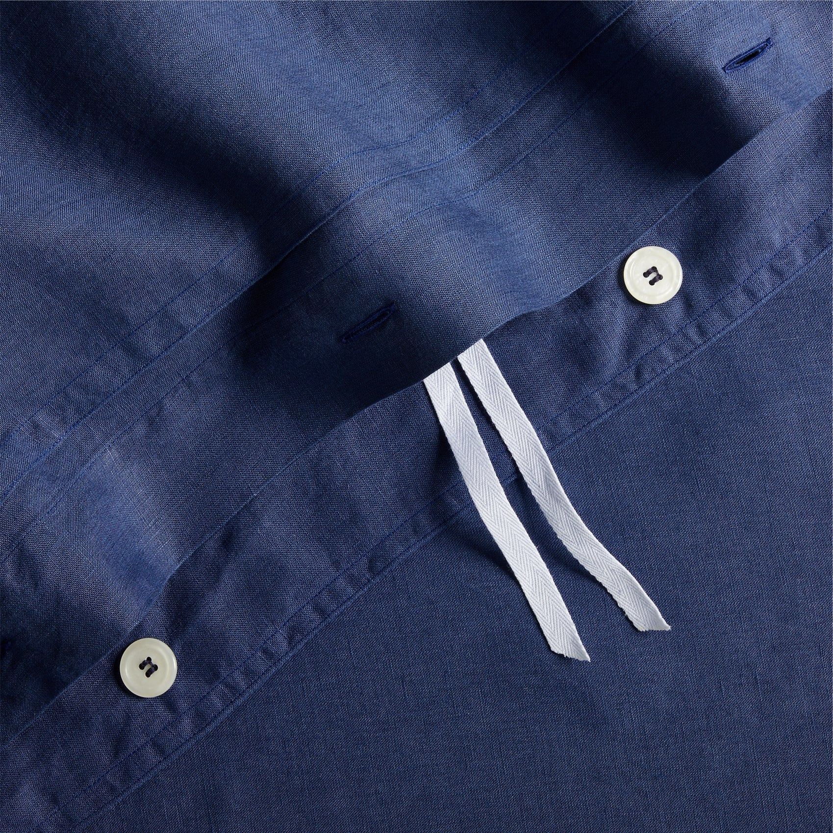 Navy blue washed linen duvet cover with white buttons, double-needle stitching, and white corner ties.
