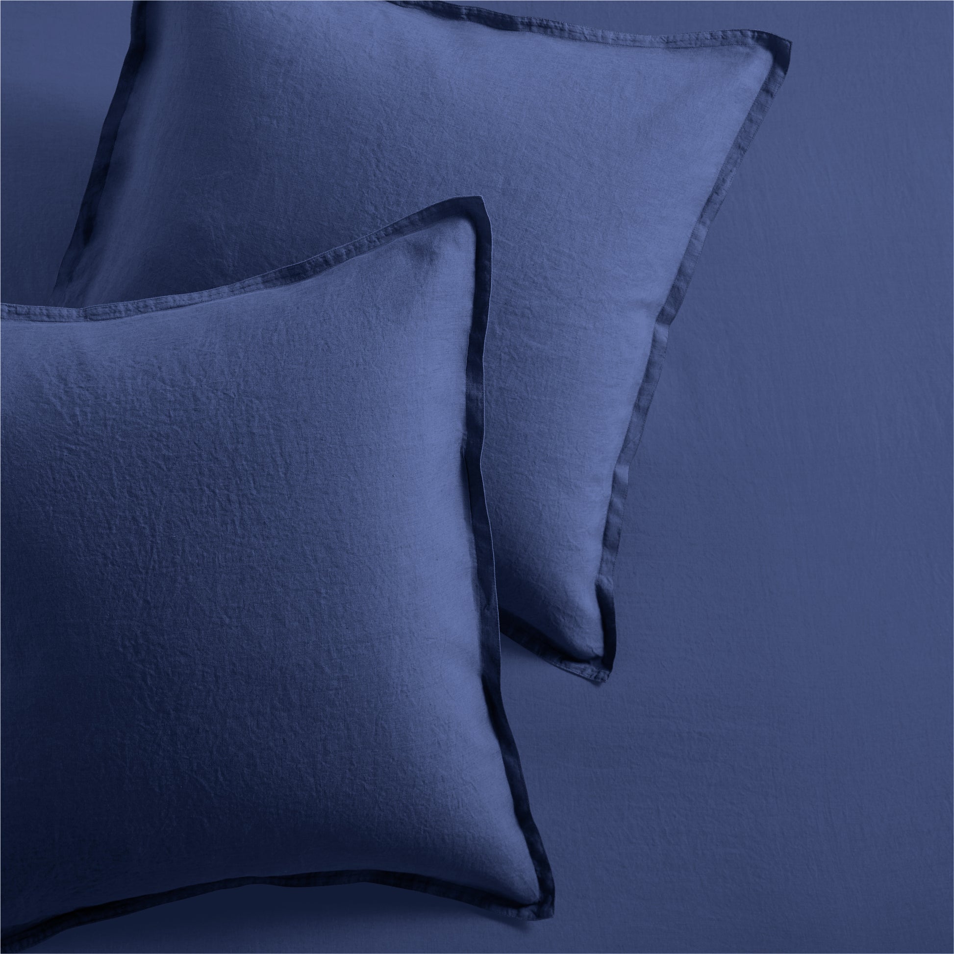 Two navy blue washed linen pillow shams with 2" flange and double-needle stitching.