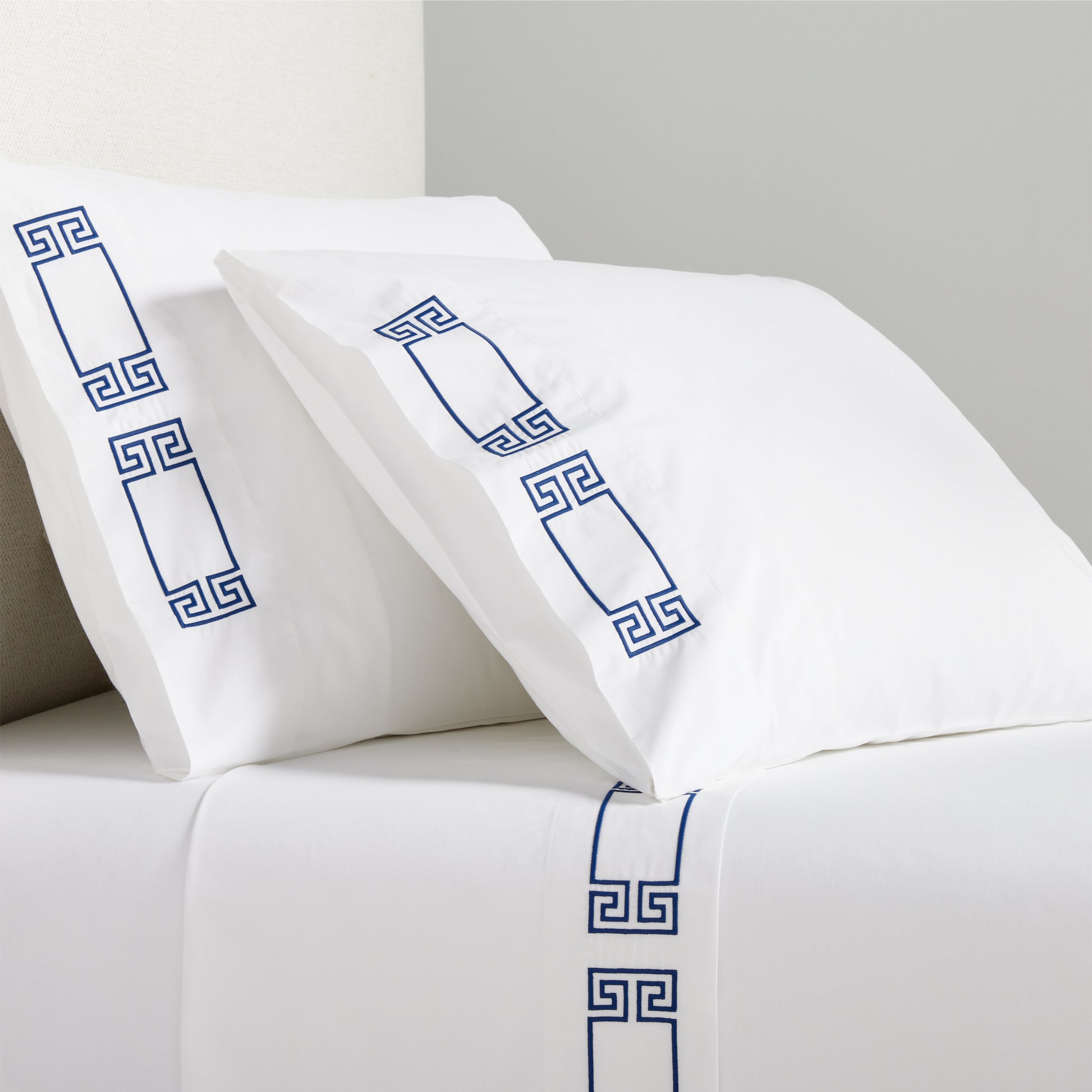 White percale sheet set with navy embroidered Greek key motif on pillowcases and flat sheet.