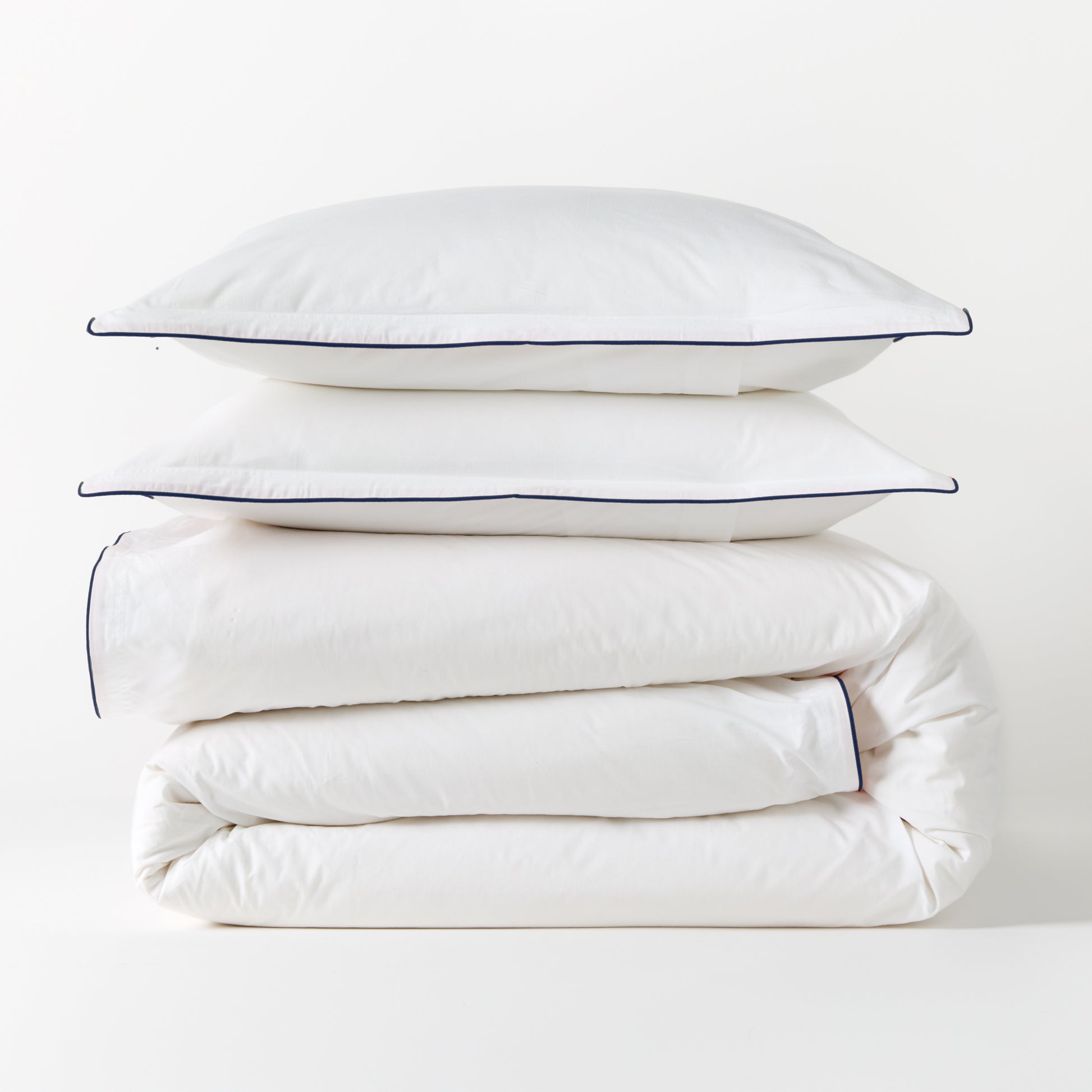 White percale duvet cover and two shams with navy piping, stacked neatly.
