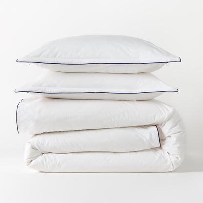 White percale duvet cover and two shams with navy piping, stacked neatly.