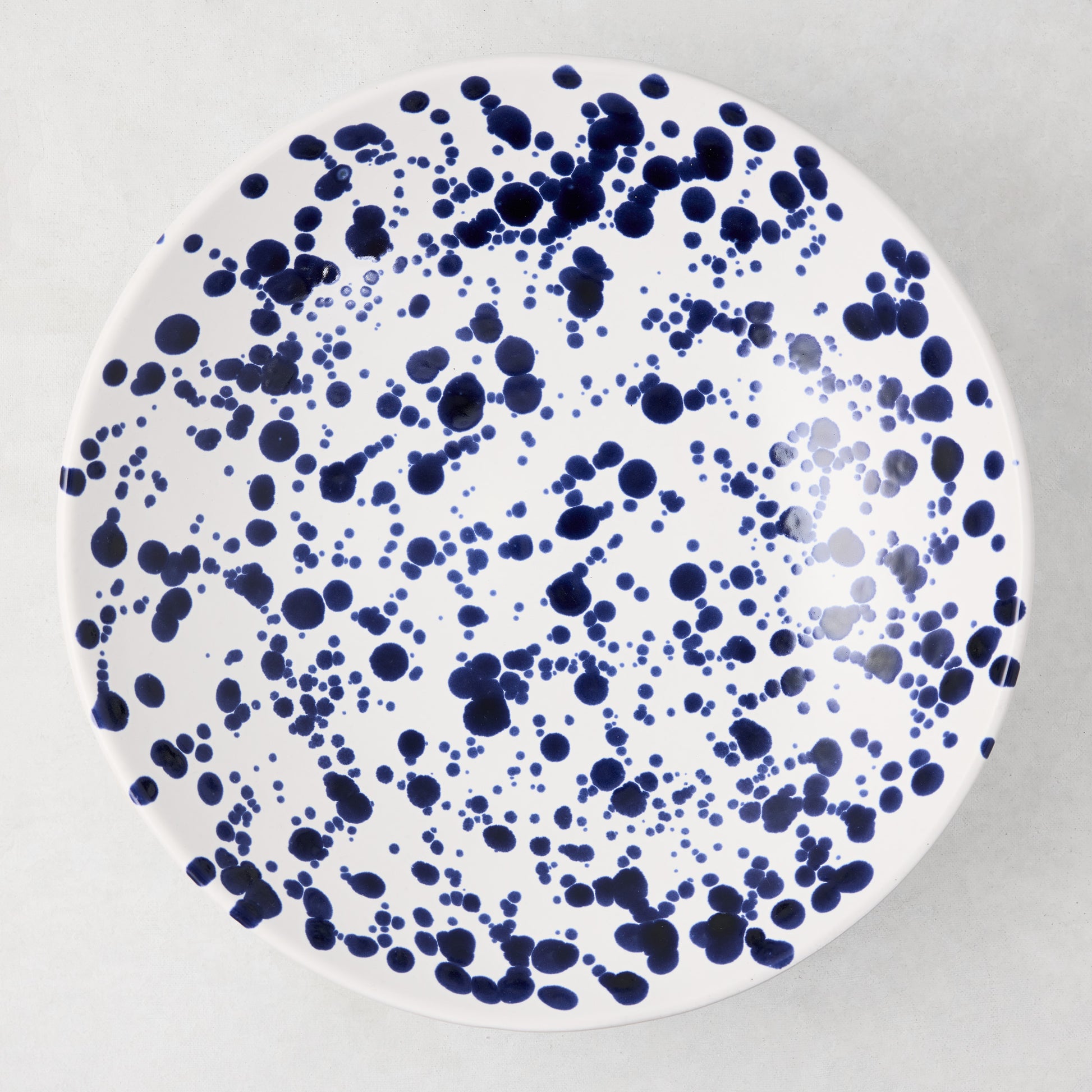 Navy blue splatter stoneware serve bowl, 12" diameter, white with hand-splattered navy dots.