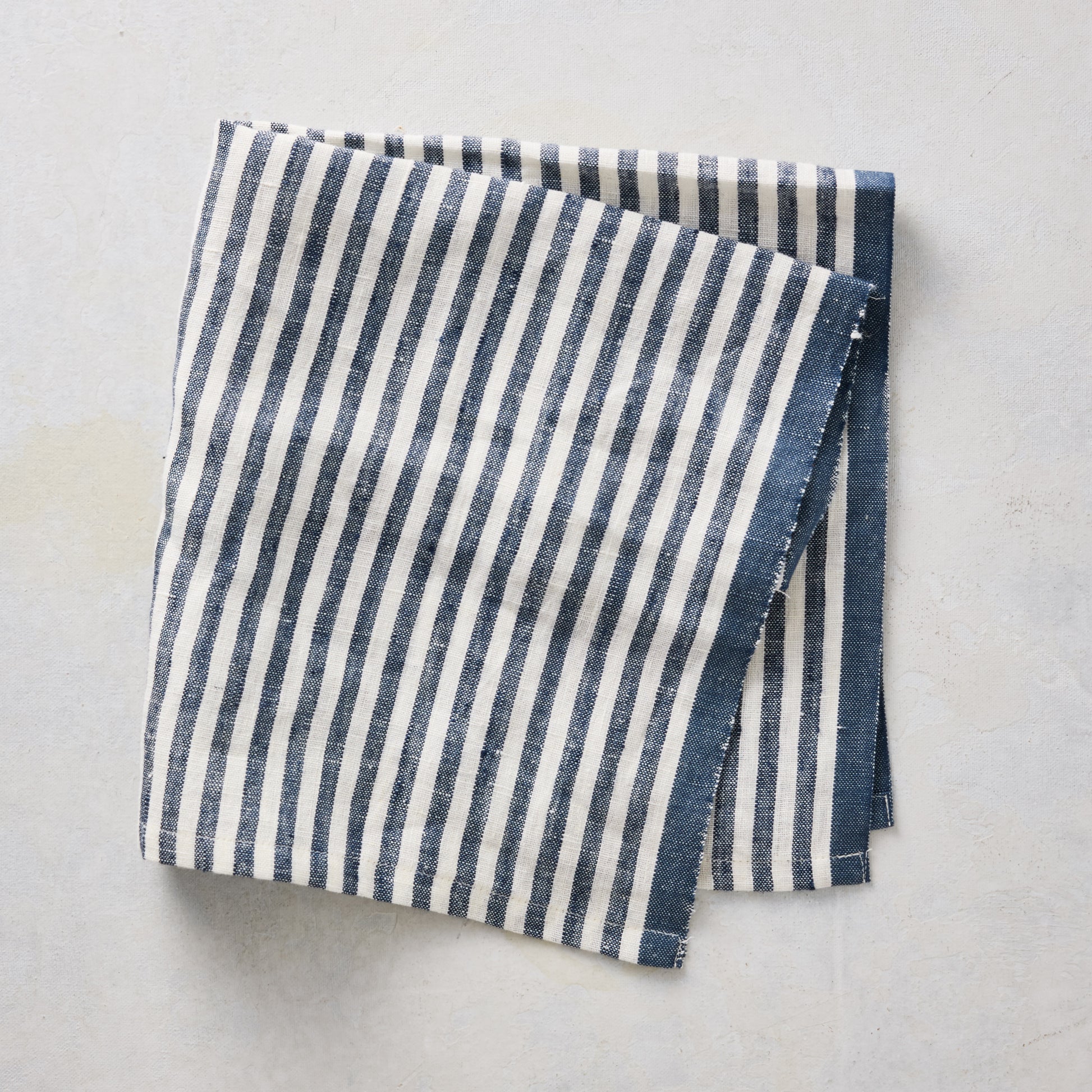 21-inch square cotton napkin with navy blue ticking stripes on a white base and a solid navy border.