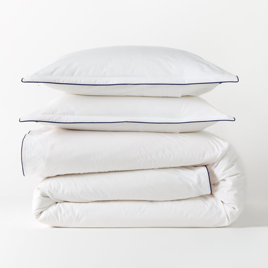 White percale duvet cover and two shams with navy piping, stacked neatly.